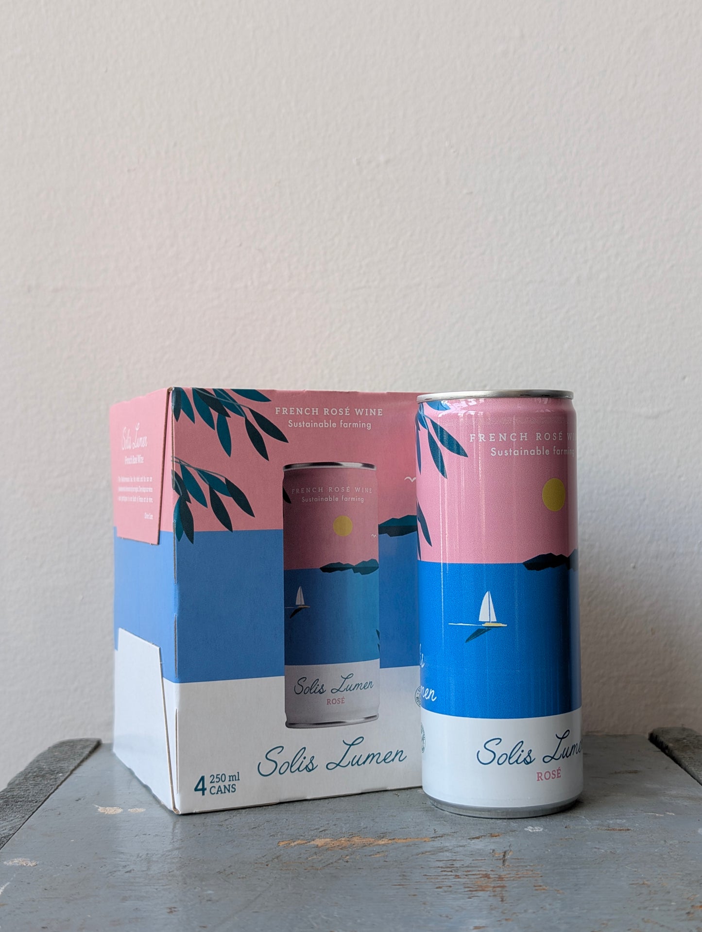 One can of Solis Lumin Rosé in front of a four pack Solis Lumin Rosé cans with a matching packaging box on a gray surface.
